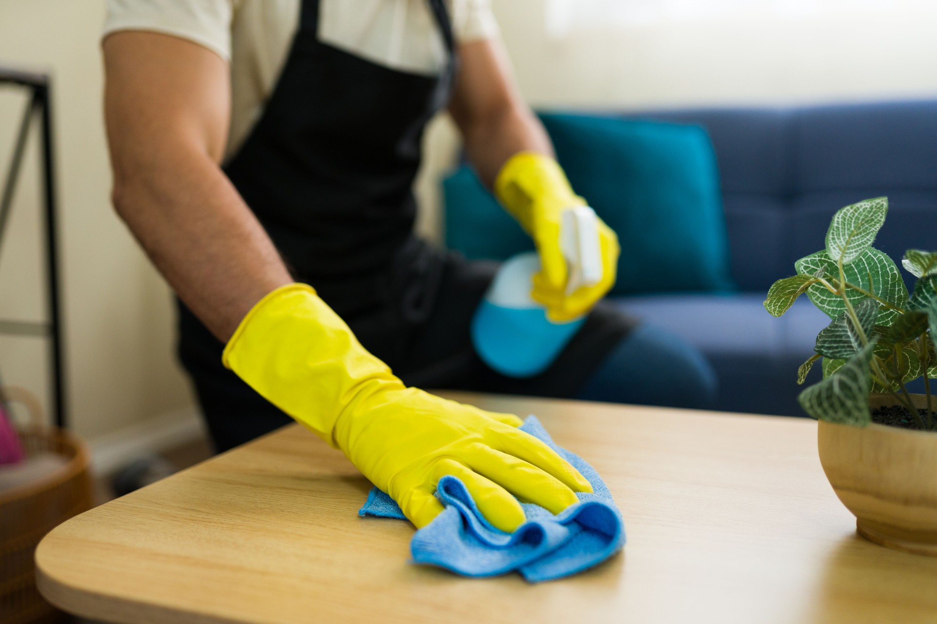Closeup of a man cleaning wooden table with disinfectant spray and microfiber cloth